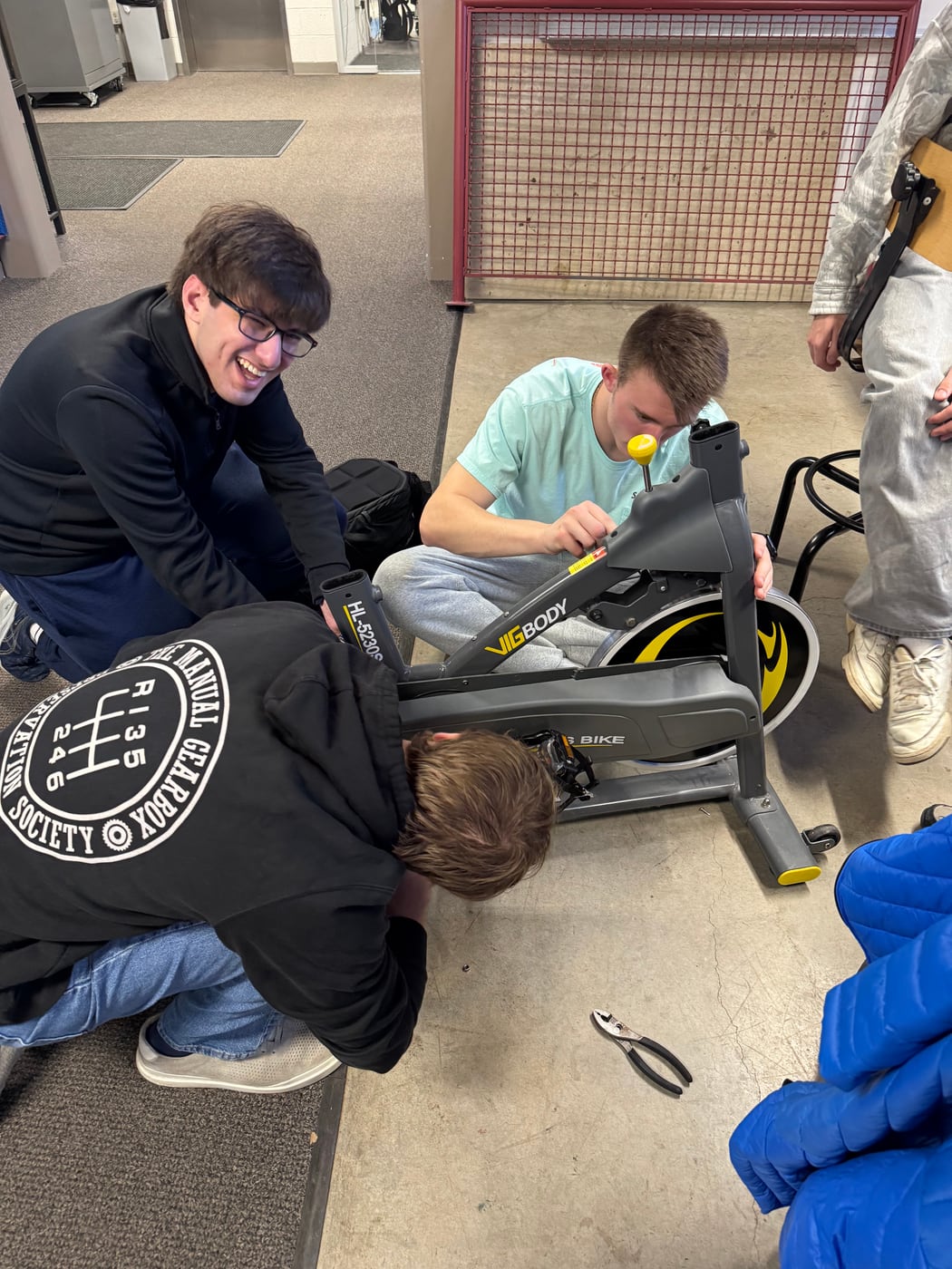Two club members taking apart an exercise bike with hand tools.
