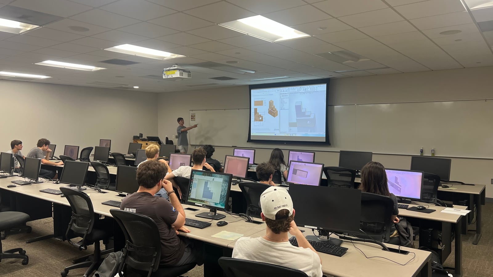 Max pointing at a projected SolidWorks screen while students follow along at computers.