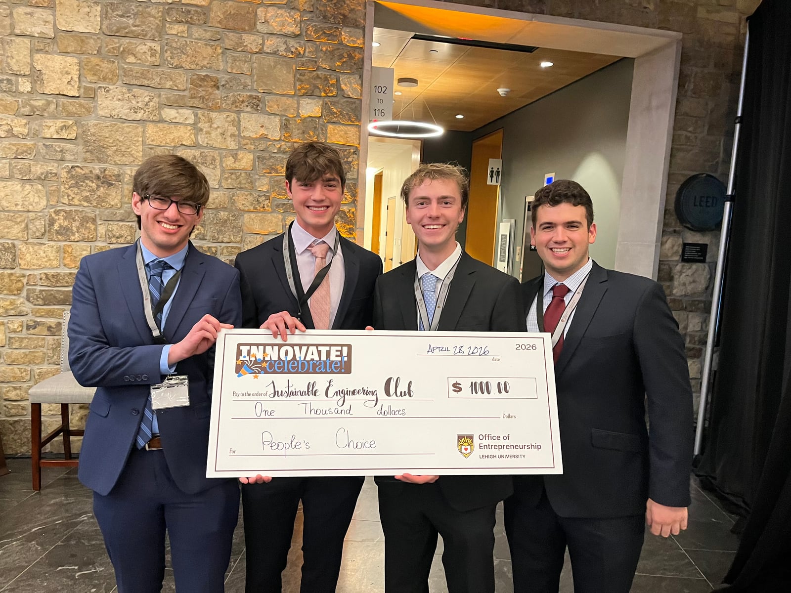 Four club members in suits holding a one thousand dollar People's Choice cheque at Innovation Alley.